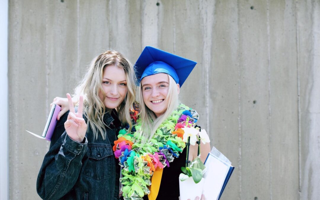 A young woman with blonde hair in a graduation gown and hat stands next to another woman with blonde hair - the two appear to be related. Supporting women and girls in STEM is important to business coaches Betty and Glorie.
